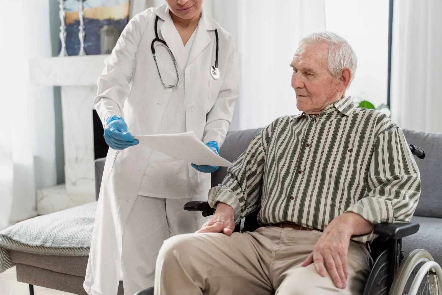 Older man seated at home looking over paperwork held by a care professional